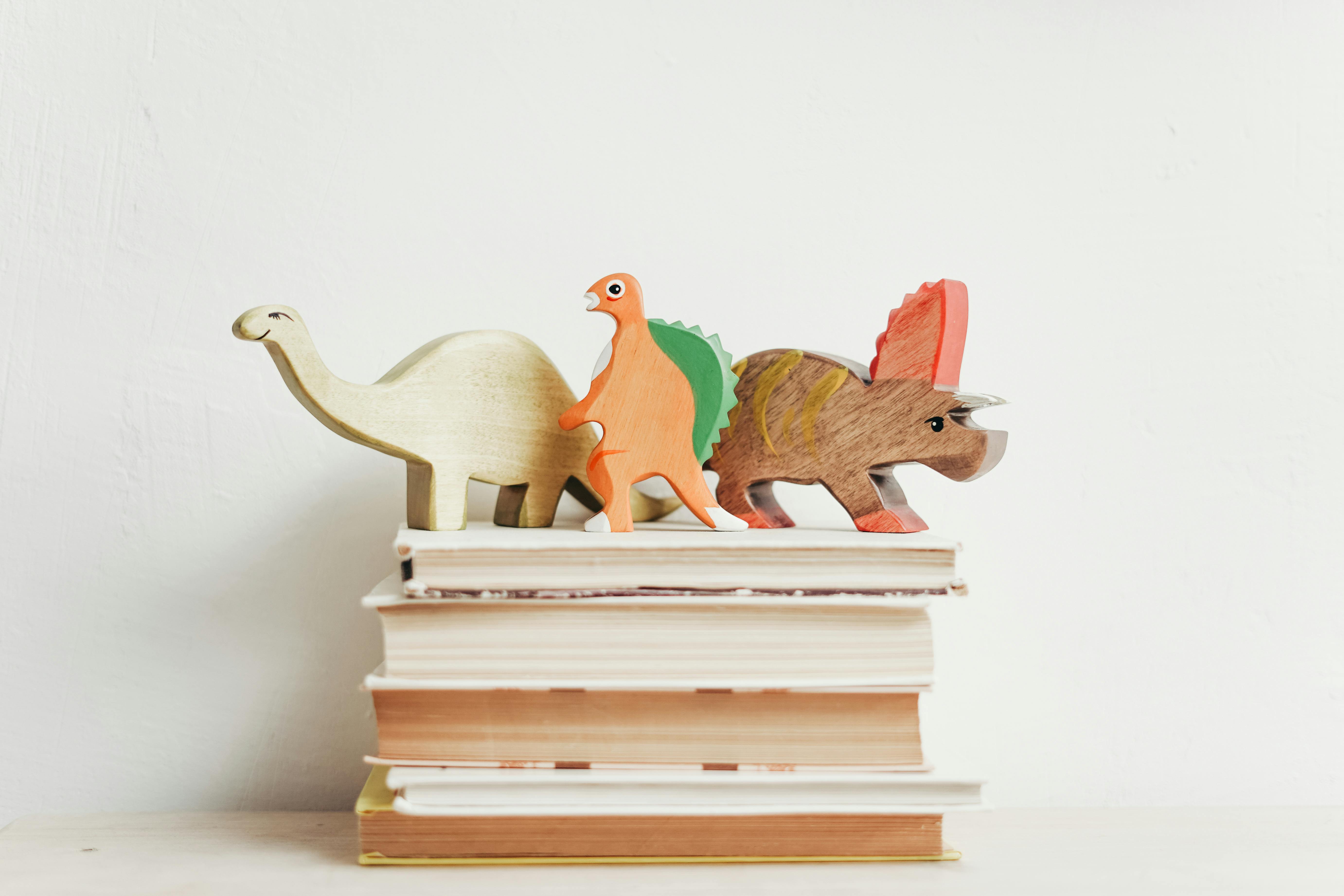 pexels-photo-3661193-3661193 Colorful wooden dinosaurs on top of a stack of hardcover books on a light background.